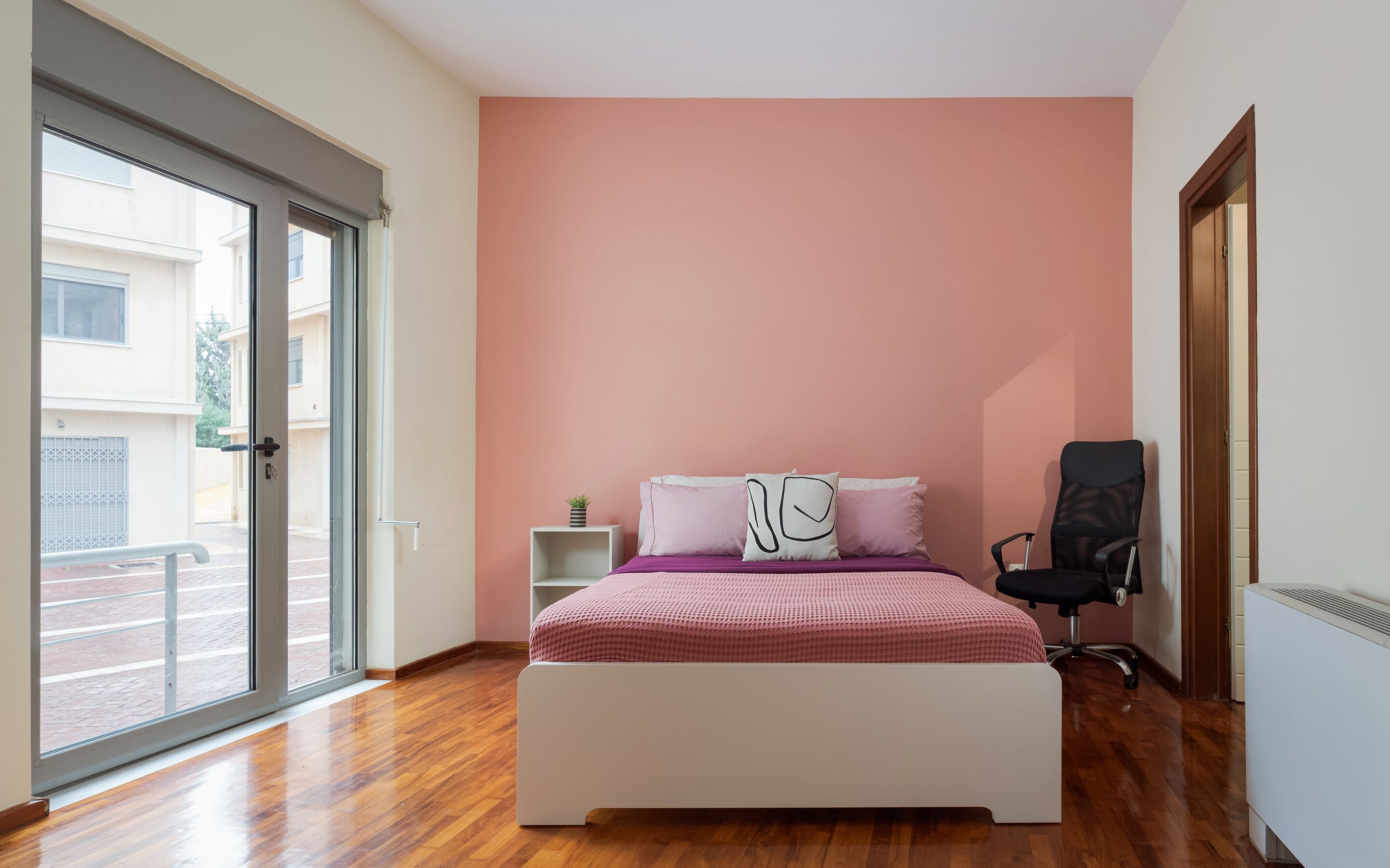 A bedroom with a bed, a chair, a nightstand, and a window.