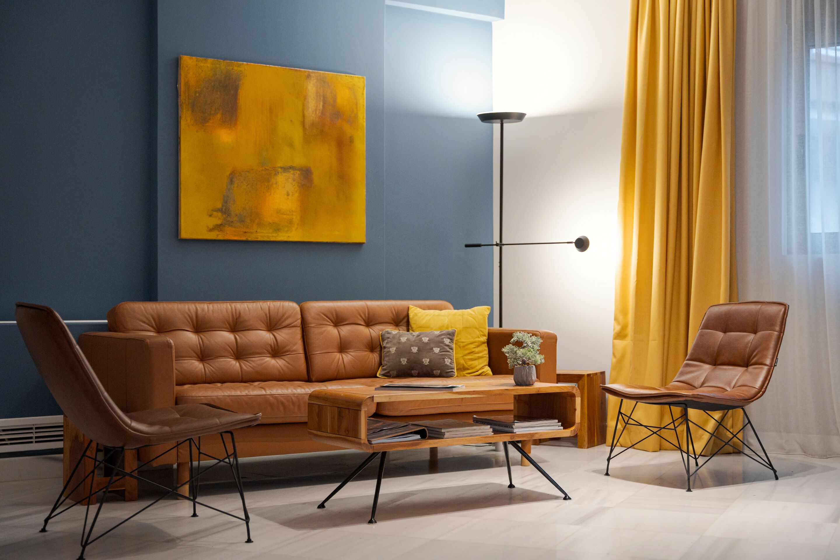 A modern living room with a brown leather sofa, two leather armchairs, a coffee table, and a floor lamp.