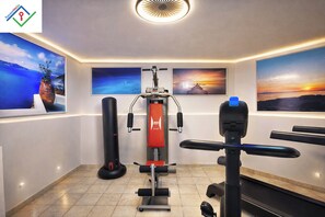 Un gimnasio con equipamiento de ejercicio, incluyendo una prensa de banca y un saco de boxeo, y arte decorativo en las paredes.