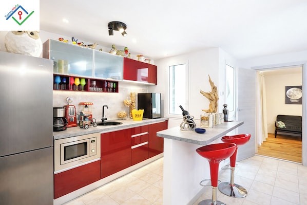 A modern kitchen with red cabinets, stainless steel appliances, and a bar area with red stools. - Villa Irene | NEW Luxury Villa with Private Pool, Jacuzzi & Sea View (Chioma)