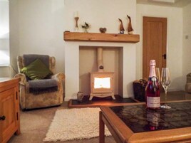 Una sala de estar acogedora con una chimenea, un aparador de madera, un sillón mullido y una mesa con una botella de vino y una copa.