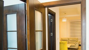 Un couloir avec une porte en bois qui donne sur un salon comprenant un canapé et une table jaune.