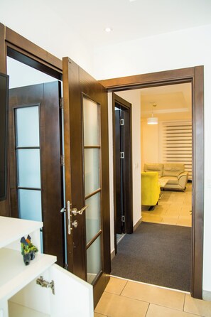 A hallway with a wooden door leading to a living area with a sofa and a yellow table. - Fully-furnished Studio Apartment at Edge (Accra)