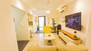 Un salon moderne avec un canapé, un fauteuil jaune, une table basse et un téléviseur à écran plat fixé au mur.