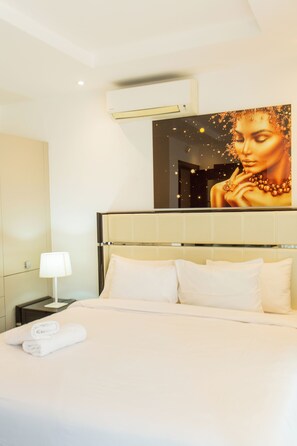 A hotel room with a large bed, a nightstand with a lamp, and a wall-mounted air conditioning unit. - Fully-furnished Studio Apartment at Edge (Accra)