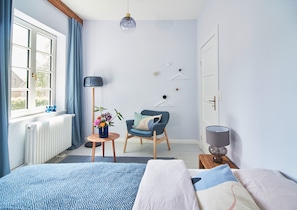 Ein Schlafzimmer mit Bett, einem Sessel, einem kleinen Tisch mit Blumenvase, einer Stehlampe und einer Heizung.