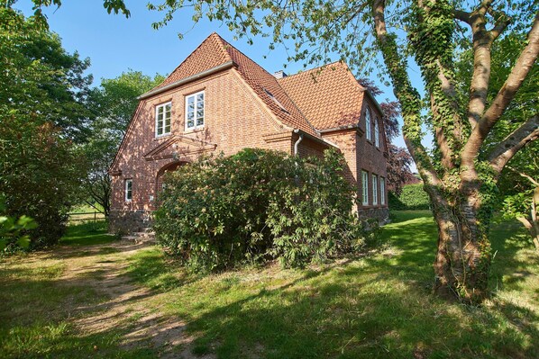 Ein Ziegelhaus mit geneigtem Dach, umgeben von viel Grün und blauem Himmel.