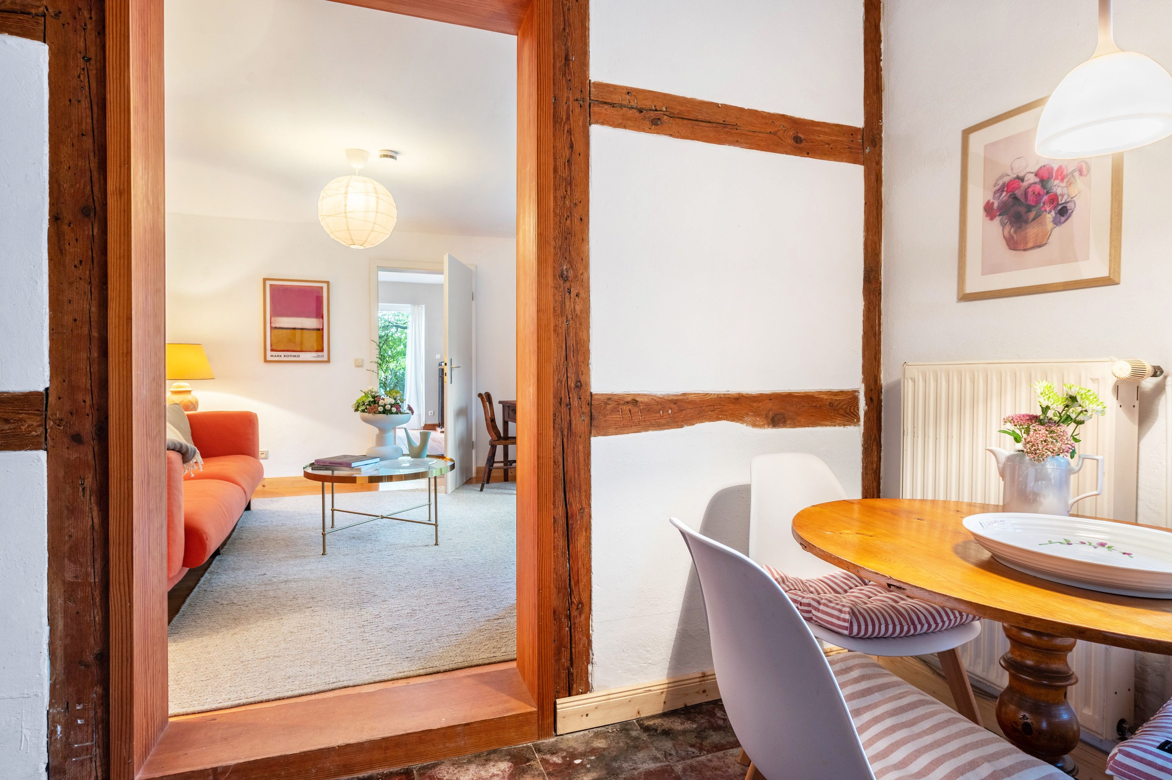 Ein Zimmer mit einer Holztür, einem Esstisch mit Stühlen, einem Sofa, einer Lampe und einem Gemälde an der Wand.