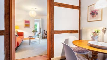 Ein Zimmer mit einer Holztür, einem Esstisch mit Stühlen, einem Sofa, einer Lampe und einem Gemälde an der Wand.