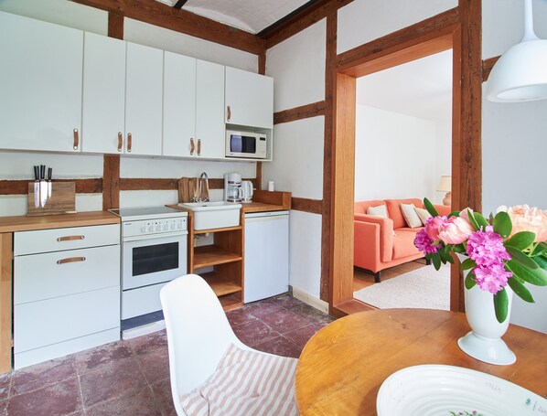 A compact kitchen with white cabinets, a wooden countertop, and a dining area with a table and chair.