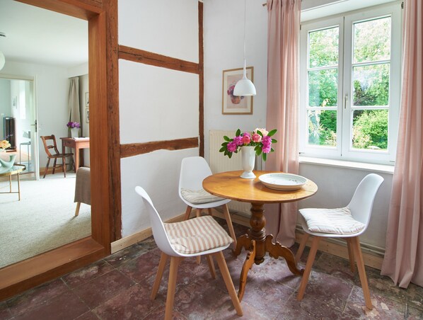 Ein Essbereich mit einem runden Holztisch, vier Stühlen, einer Blumenvase und einem fenster mit Vorhängen.