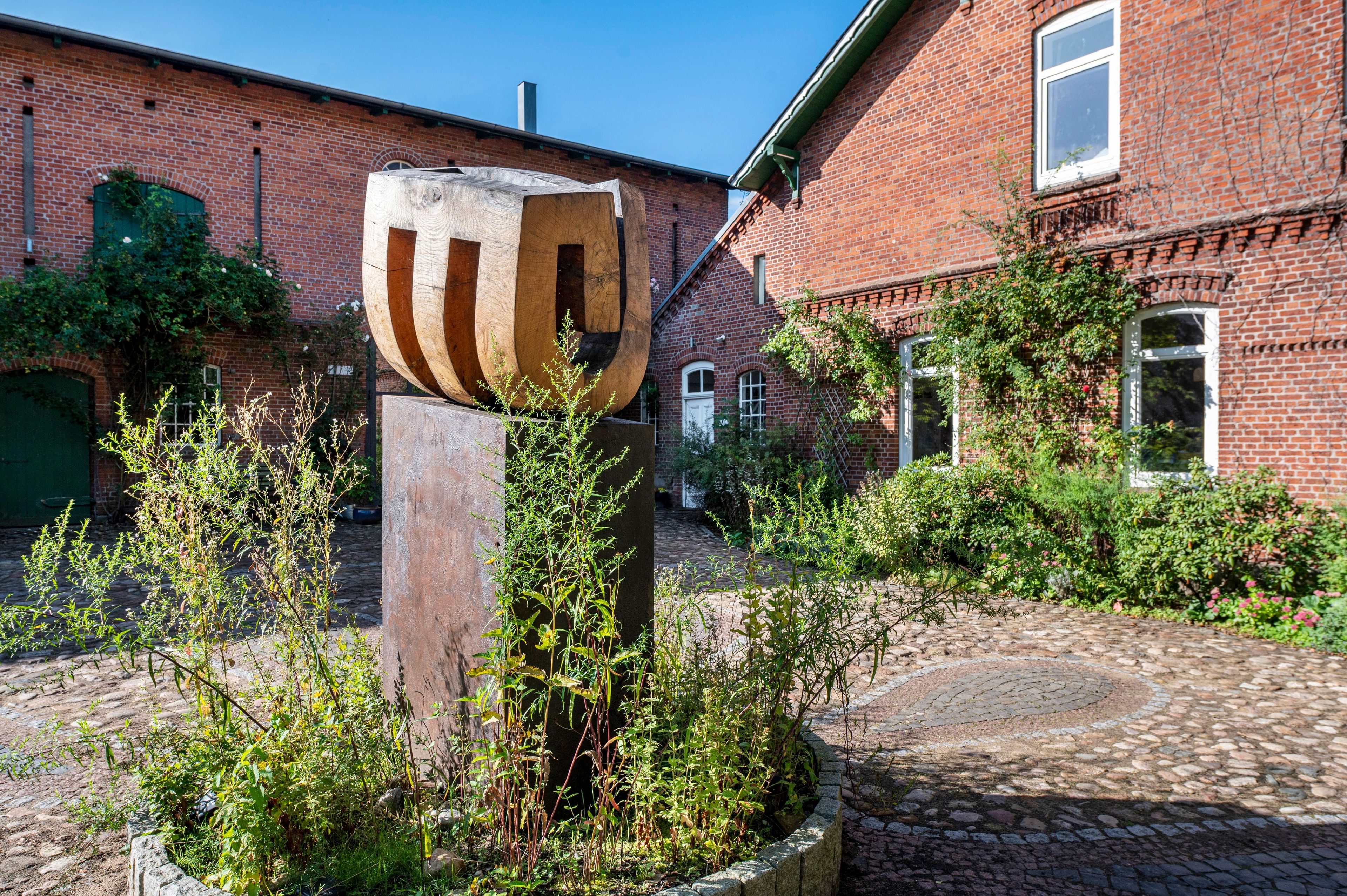 Ein Innenhof mit einer großen Holzskulptur, einem Backsteingebäude und einem Kopfsteinpflasterweg.