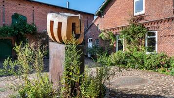 Ein Innenhof mit einer großen Holzskulptur, einem Backsteingebäude und einem Kopfsteinpflasterweg.