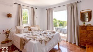 A bedroom with a bed, a dresser, a mirror, and a balcony with curtains. - Villa ARNELLA by Abahana Villas (Teulada)