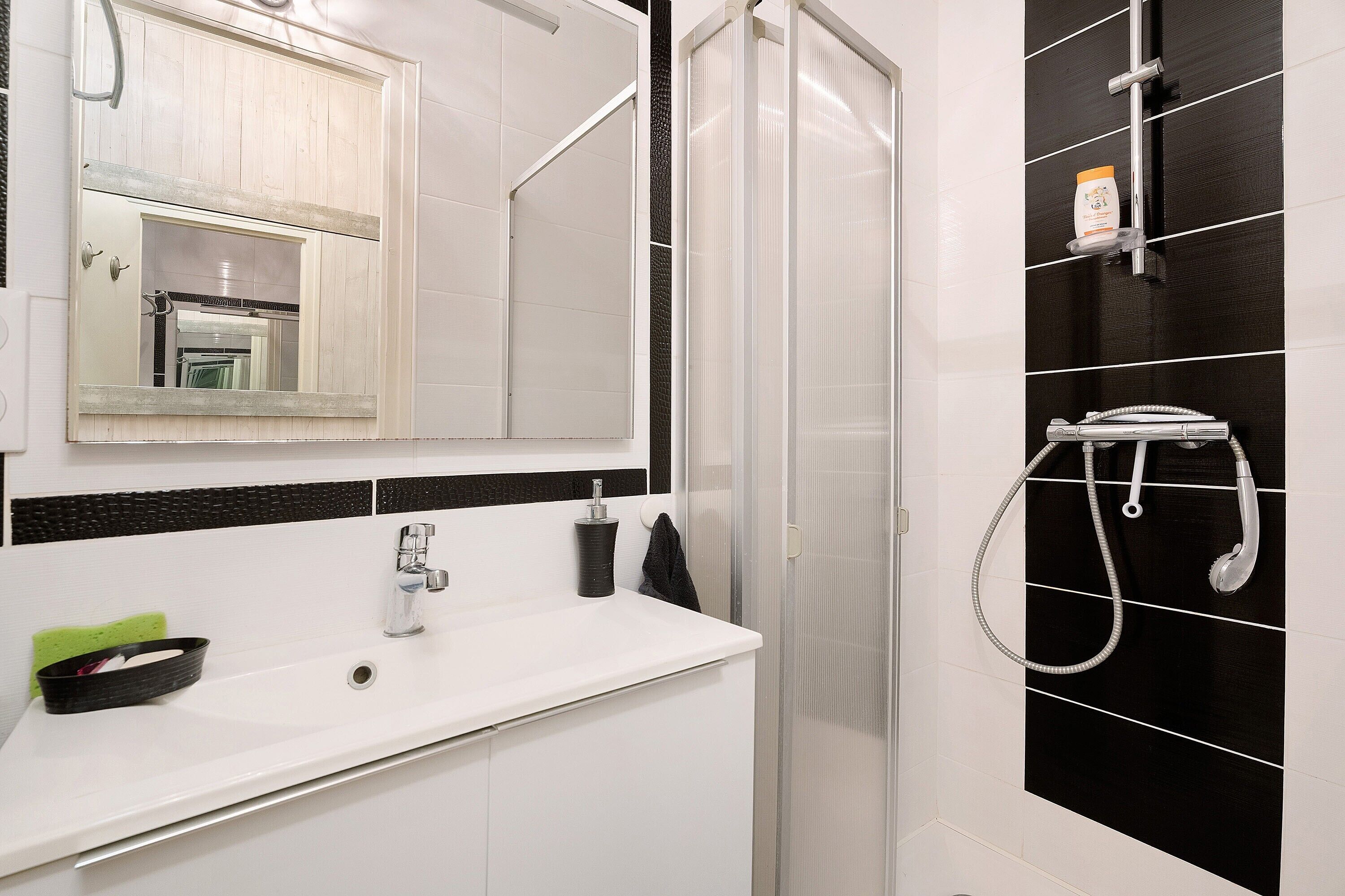 Een badkamer met een wit wastafel, een spiegel, een douche met een handdouche en een handdoekrek.