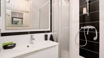 Een badkamer met een wit wastafel, een spiegel, een douche met een handdouche en een handdoekrek.