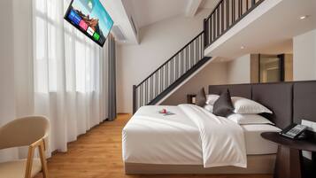 A modern hotel room with a bed, a desk, a chair, and a TV mounted on the wall.