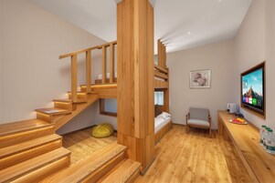 A modern interior with a wooden staircase, a bed, a chair, a desk with a computer, and a television.