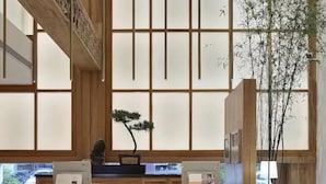 A modern reception area with a wooden reception desk, a bonsai tree, and a large window with a view of the outside. - Huangshan Old Street Garden Boutique  (Huangshan)