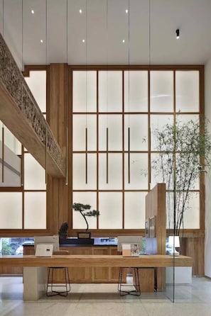 A modern reception area with a wooden reception desk, a bonsai tree, and a large window with a view of the outside. - Huangshan Old Street Garden Boutique  (Huangshan)