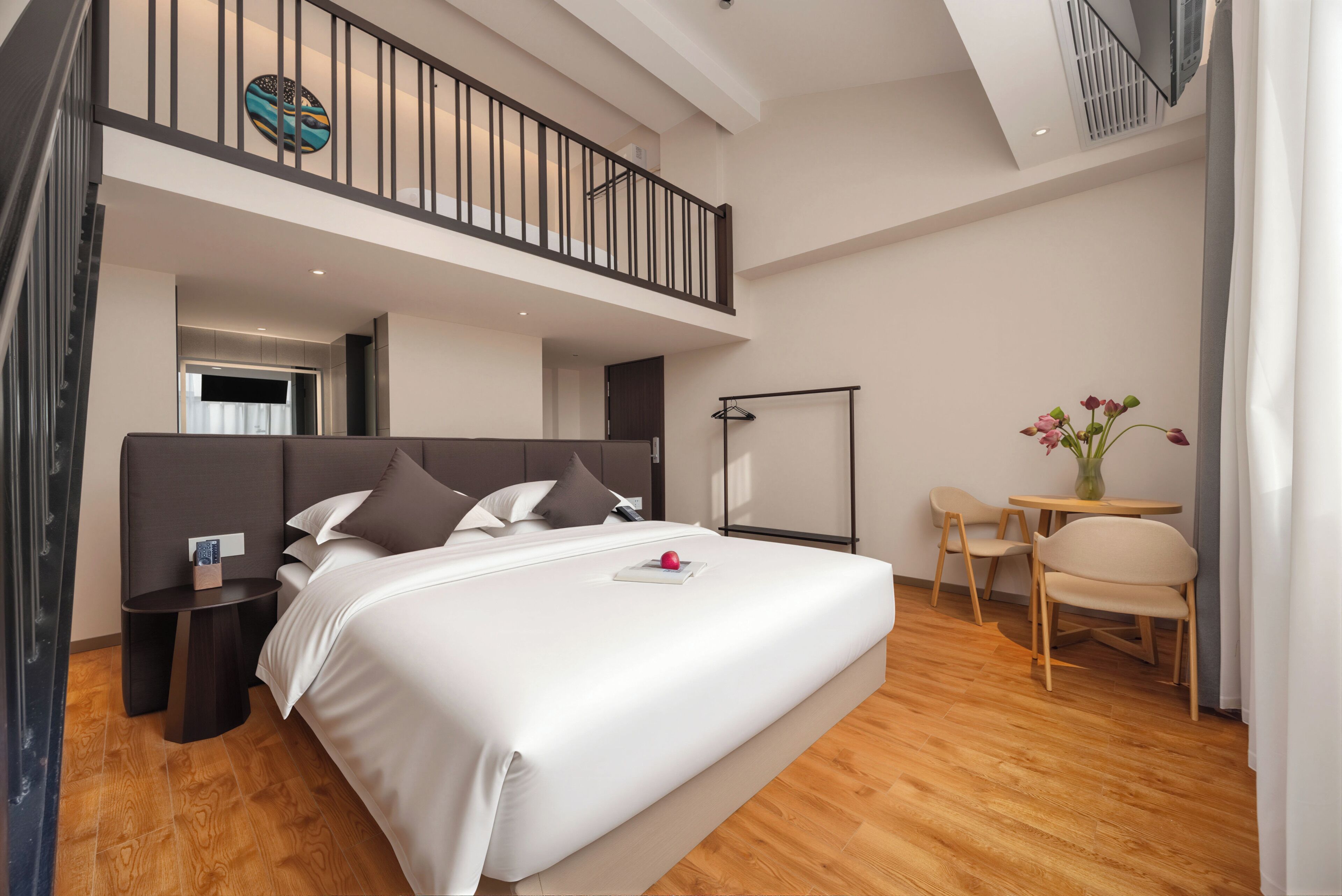A modern hotel room with a large bed, a small table, a chair, a desk, and a balcony.
