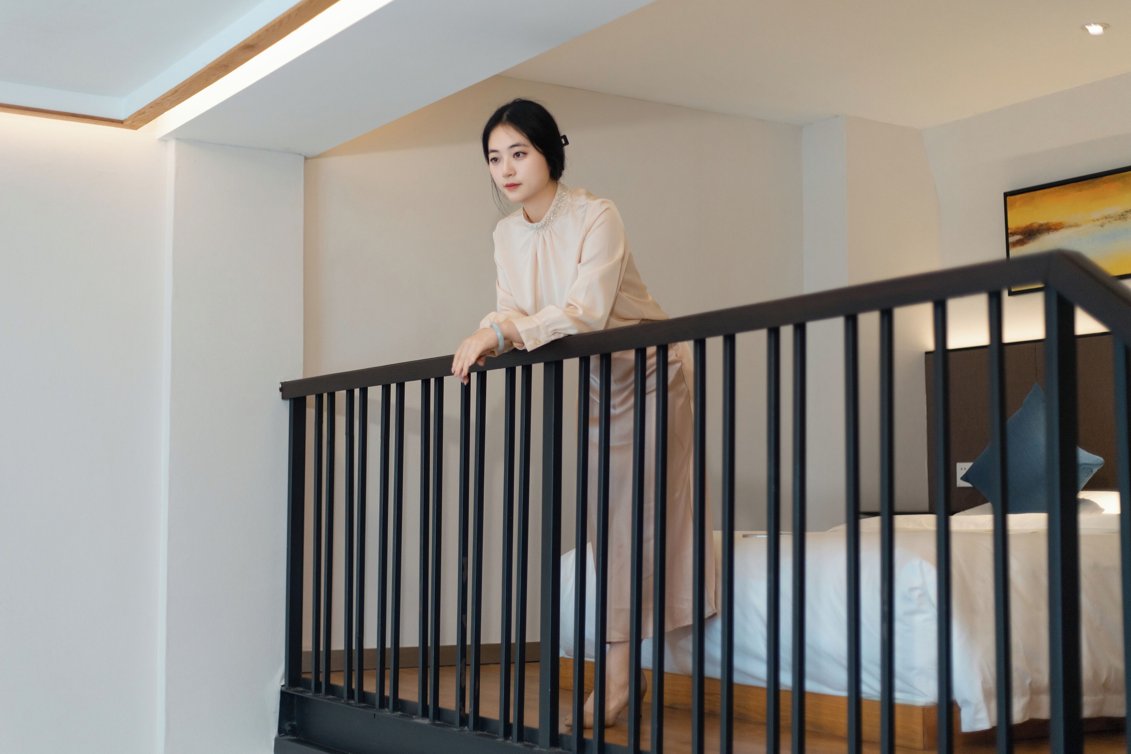 A person standing on a balcony with a bed and a painting in the background.