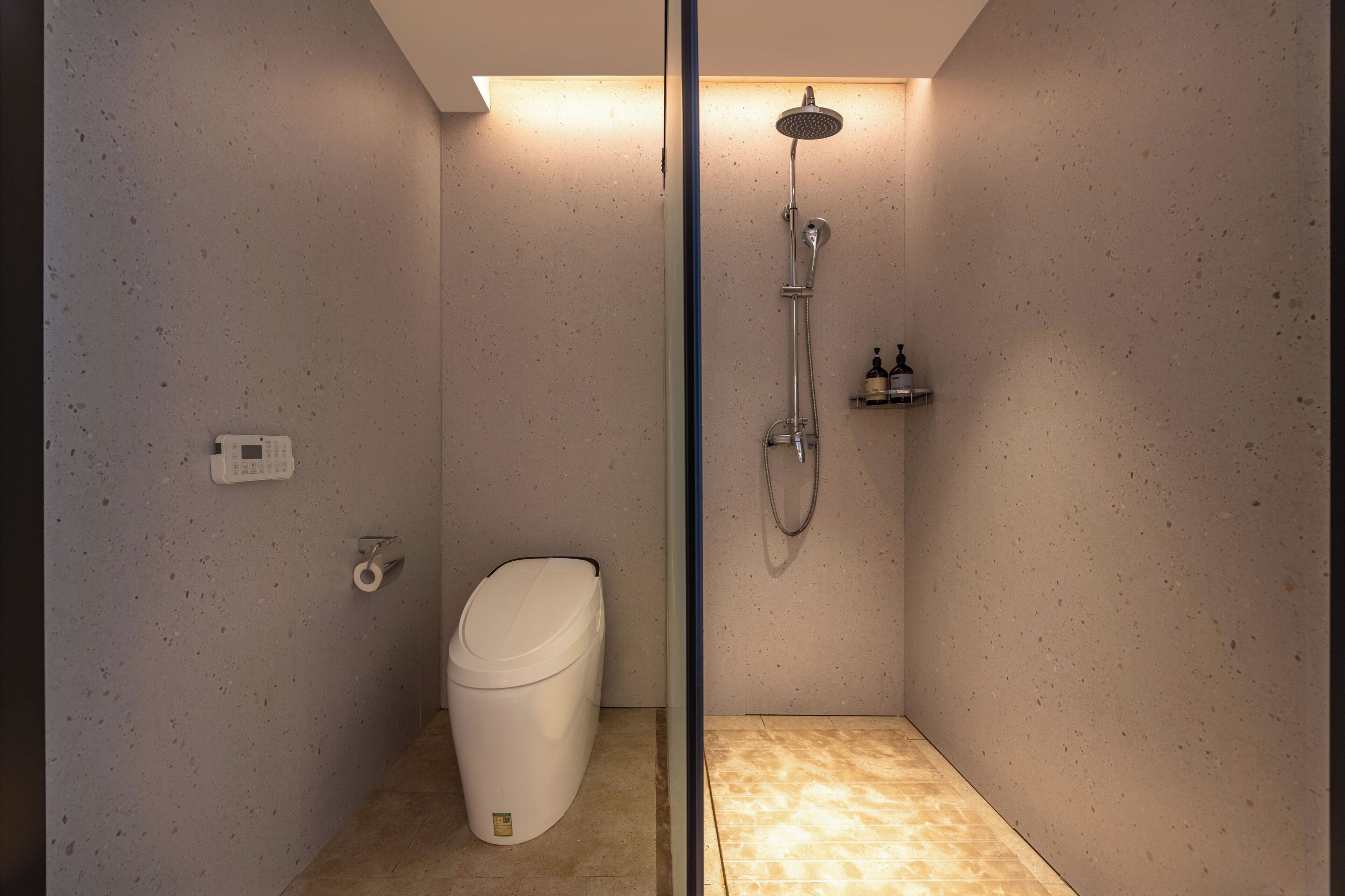 A small, modern bathroom with a shower, toilet, and a wall-mounted soap dispenser.