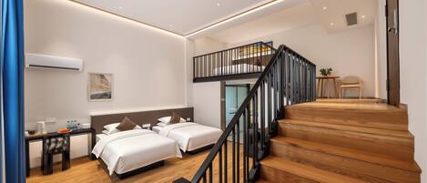 Una habitación de hotel moderna con una escalera de madera, dos camas, un escritorio y un pequeño rincón de descanso.