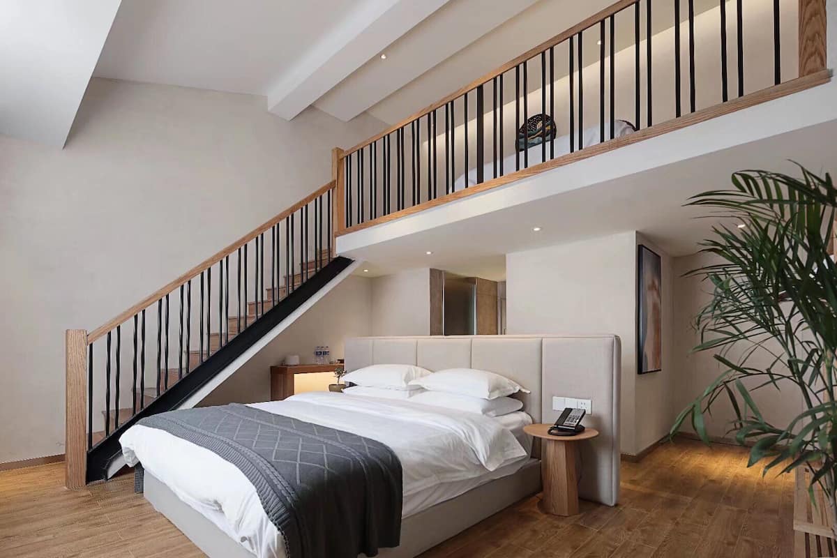 Quarto com cama grande, escada de madeira, mesa de cabeceira e um vaso com planta.