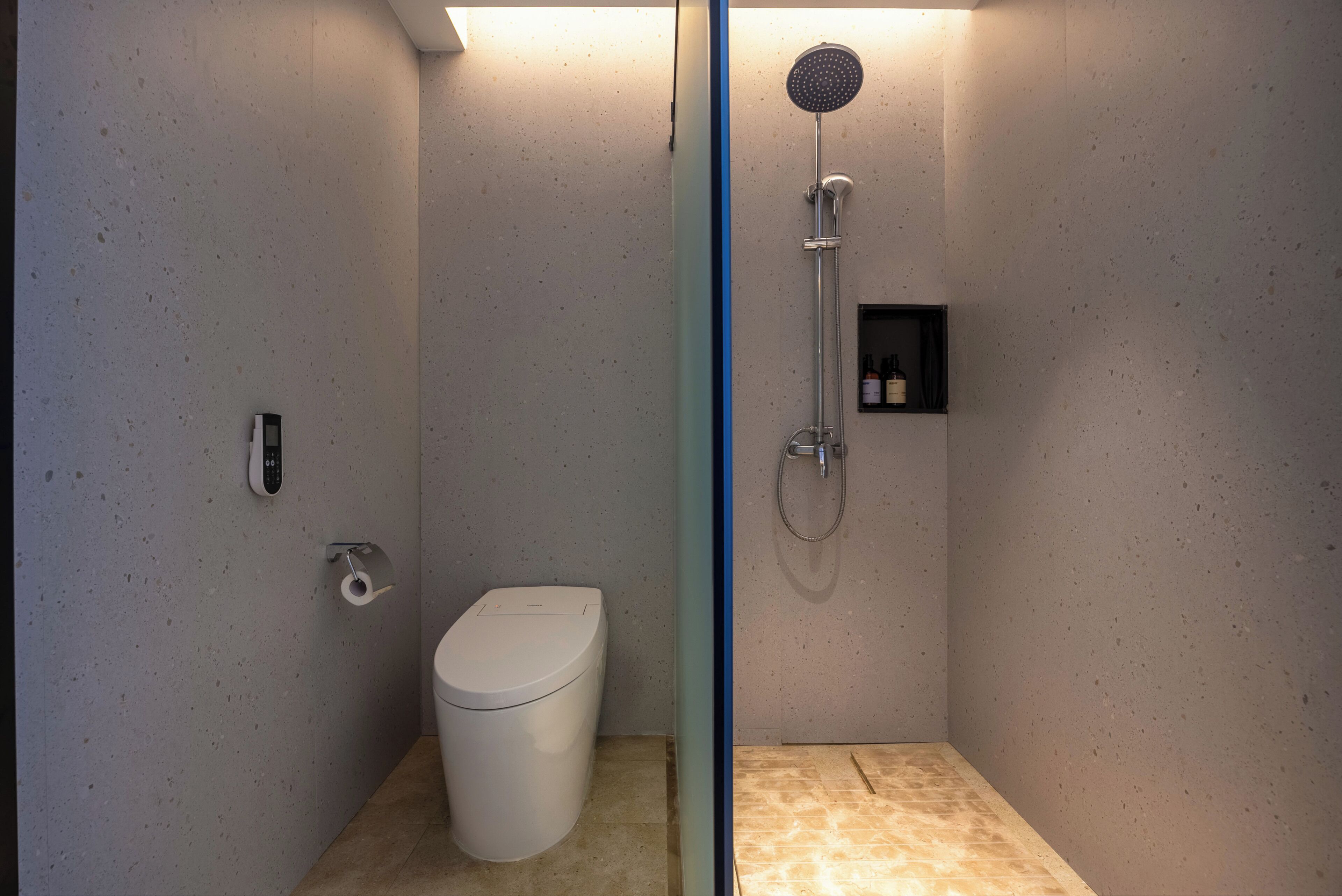Moderni kylpyhuone, jossa on wc, suihku ja pieni hylly, jossa on hygieniatuotteita.