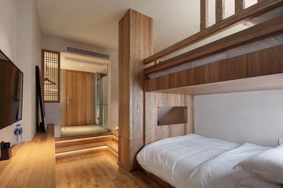 Quarto moderno com beliche, detalhes em madeira, uma pequena mesa de cabeceira e um espelho grande.