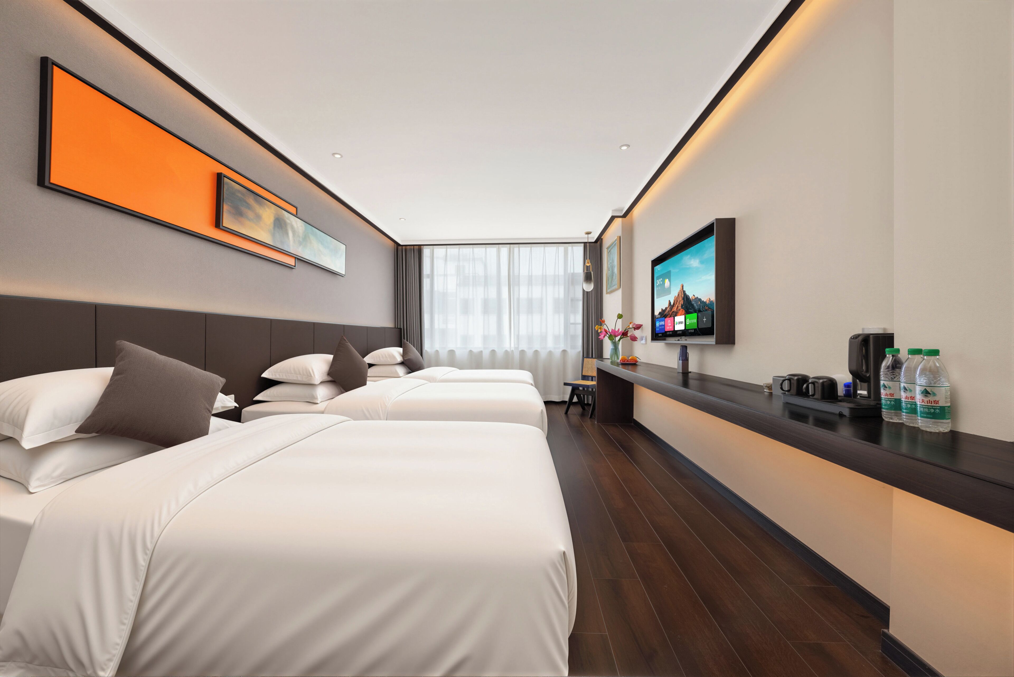 A hotel room with two beds, a flat-screen TV, a small table with a vase and bottles, and a window with curtains.