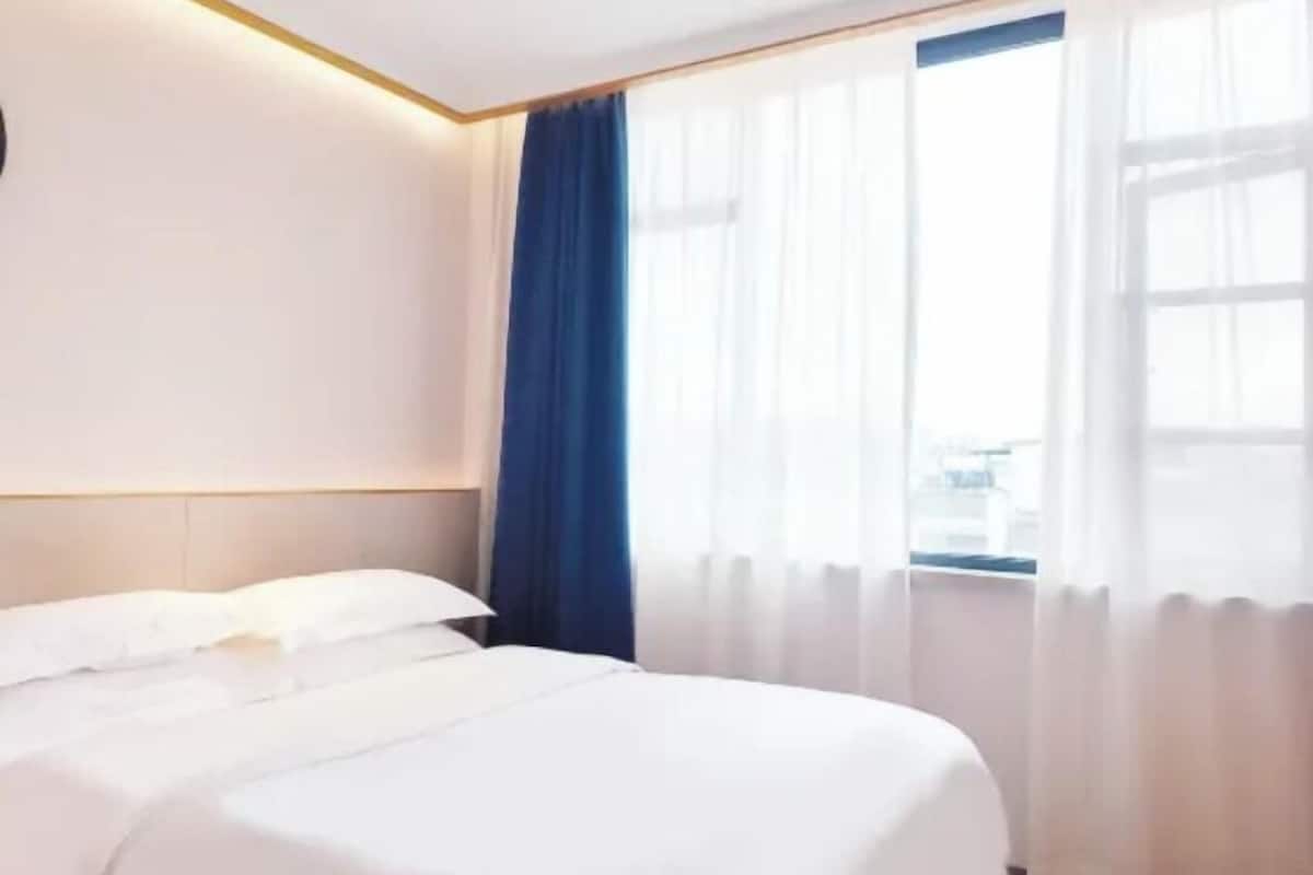 Quarto de hotel com cama, cabeceira, janela com cortinas e vista da cidade.