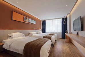 Ein Hotelzimmer mit drei Betten, einem großen Fernseher und einem Holztisch.