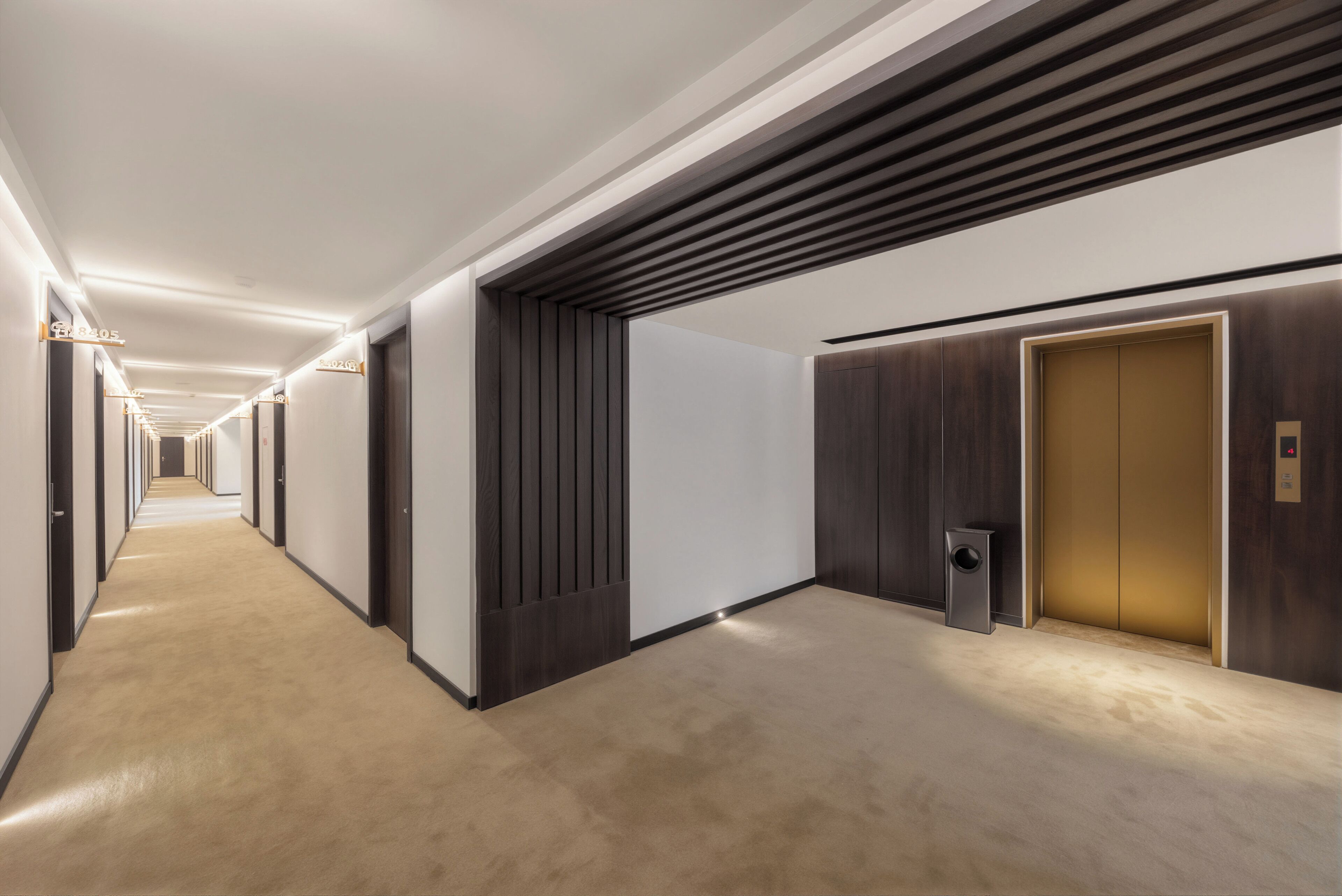 Un pasillo de hotel con una larga extensión, puertas y un ascensor.