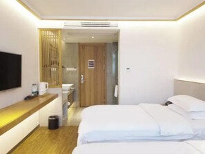 Ein Hotelzimmer mit Bett, Schreibtisch mit Stuhl, Fernseher und einem durch eine geöffnete Tür einsehbaren Badezimmer.