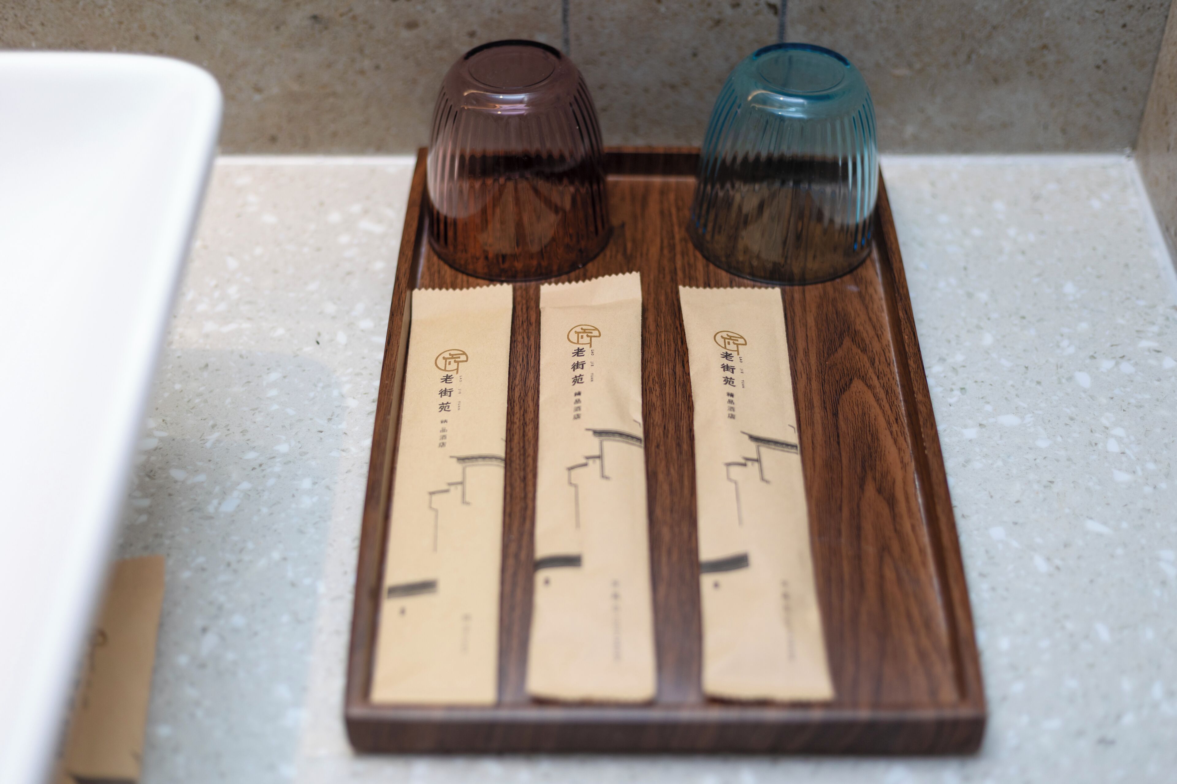 Una bandeja de madera con tres productos empacados y dos vasos sobre una encimera.