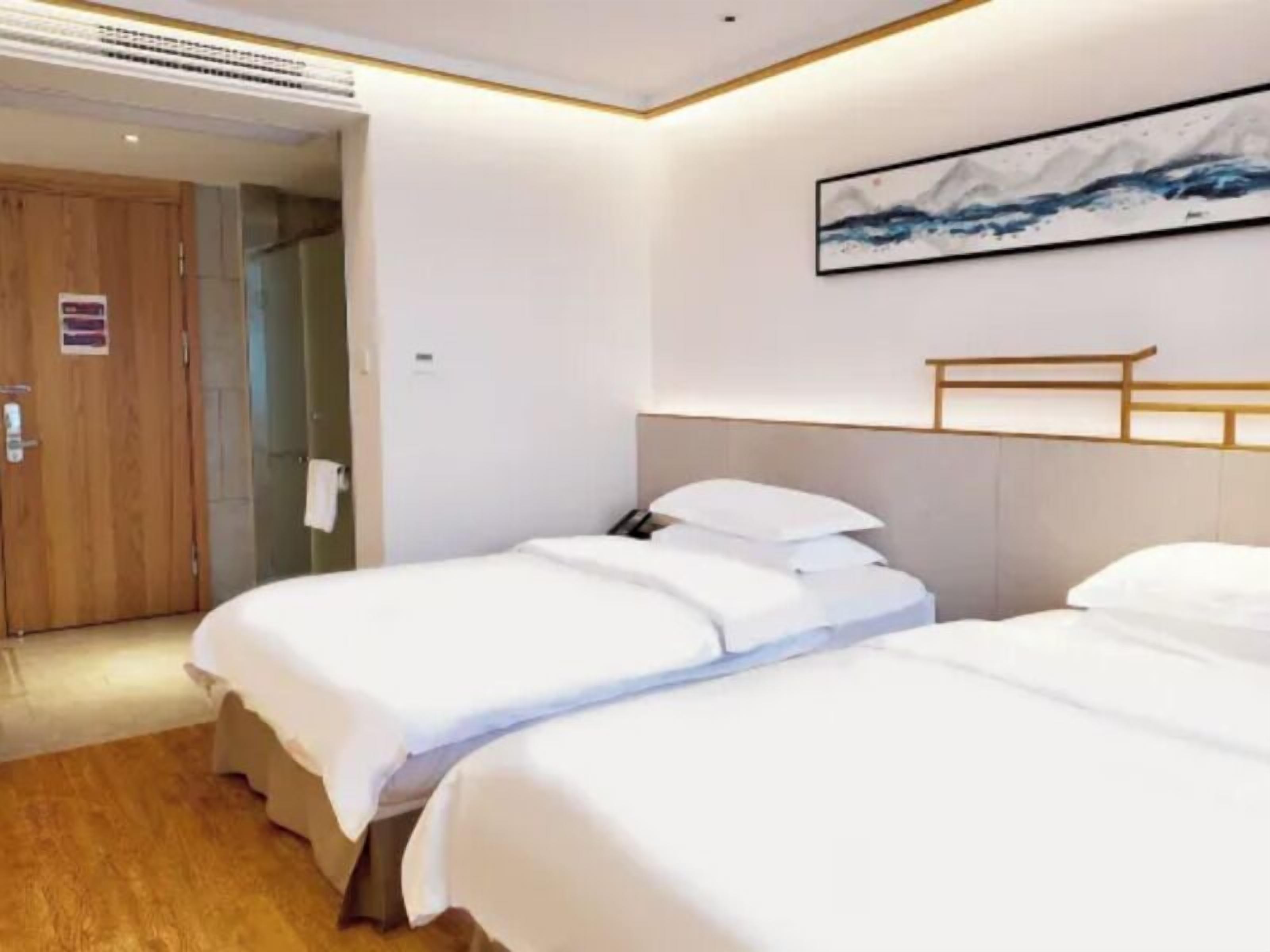 A hotel room with two beds, a wooden door, and a painting on the wall.