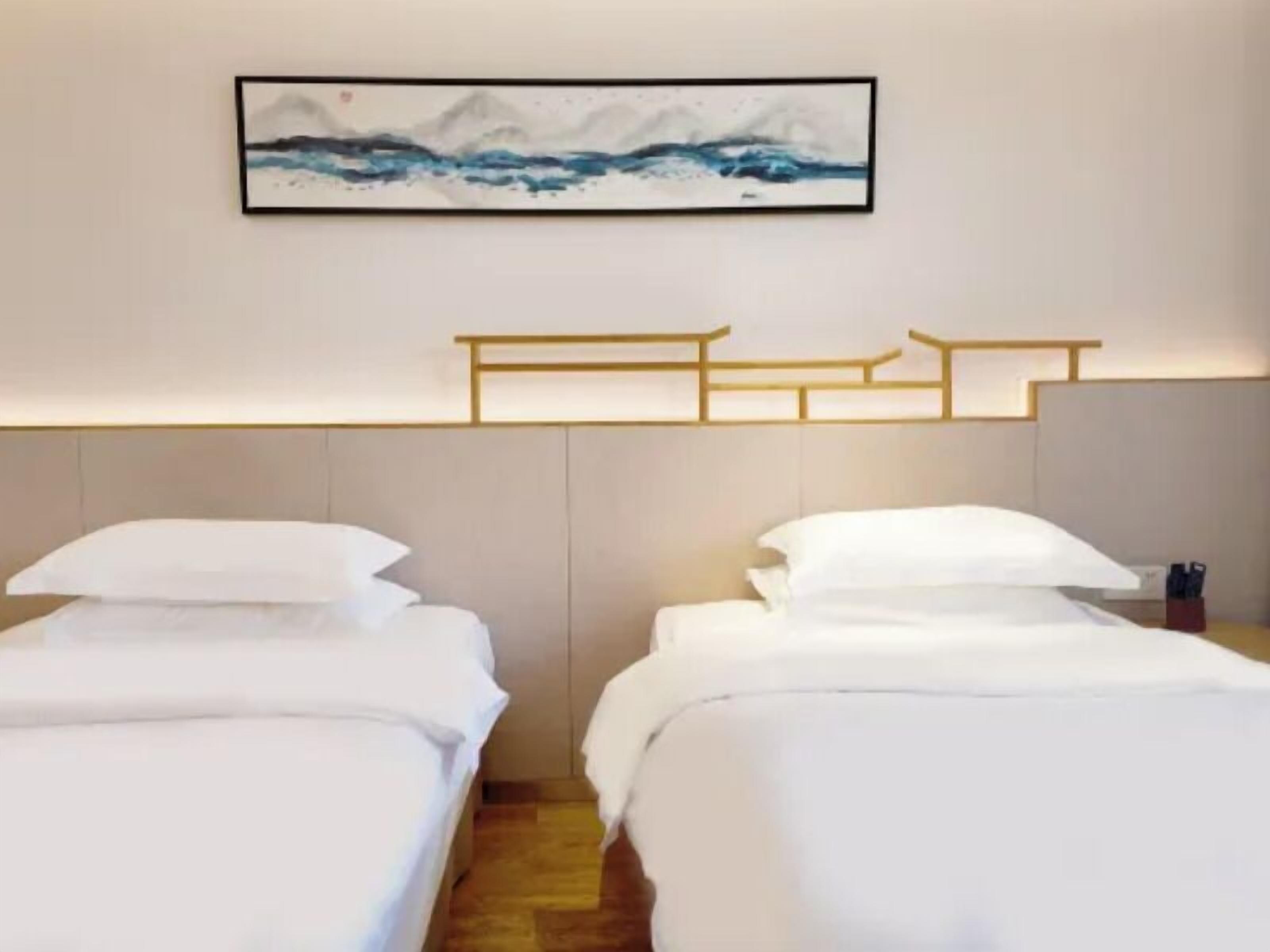 A hotel room with two beds, a wooden headboard, and a framed artwork above the beds.
