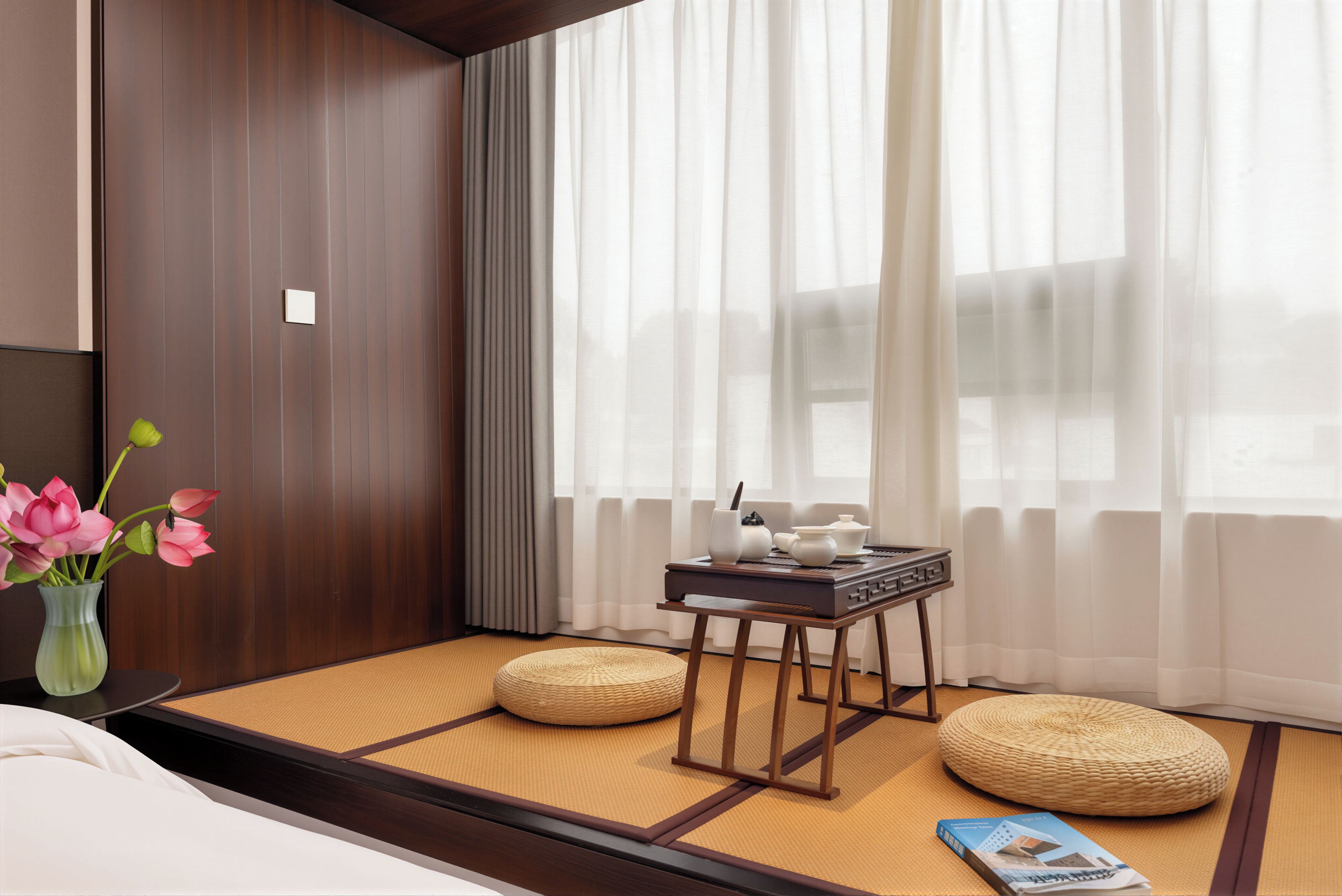 A hotel room with tatami flooring, a small wooden table with tea set, a vase with flowers, and a magazine on the floor.