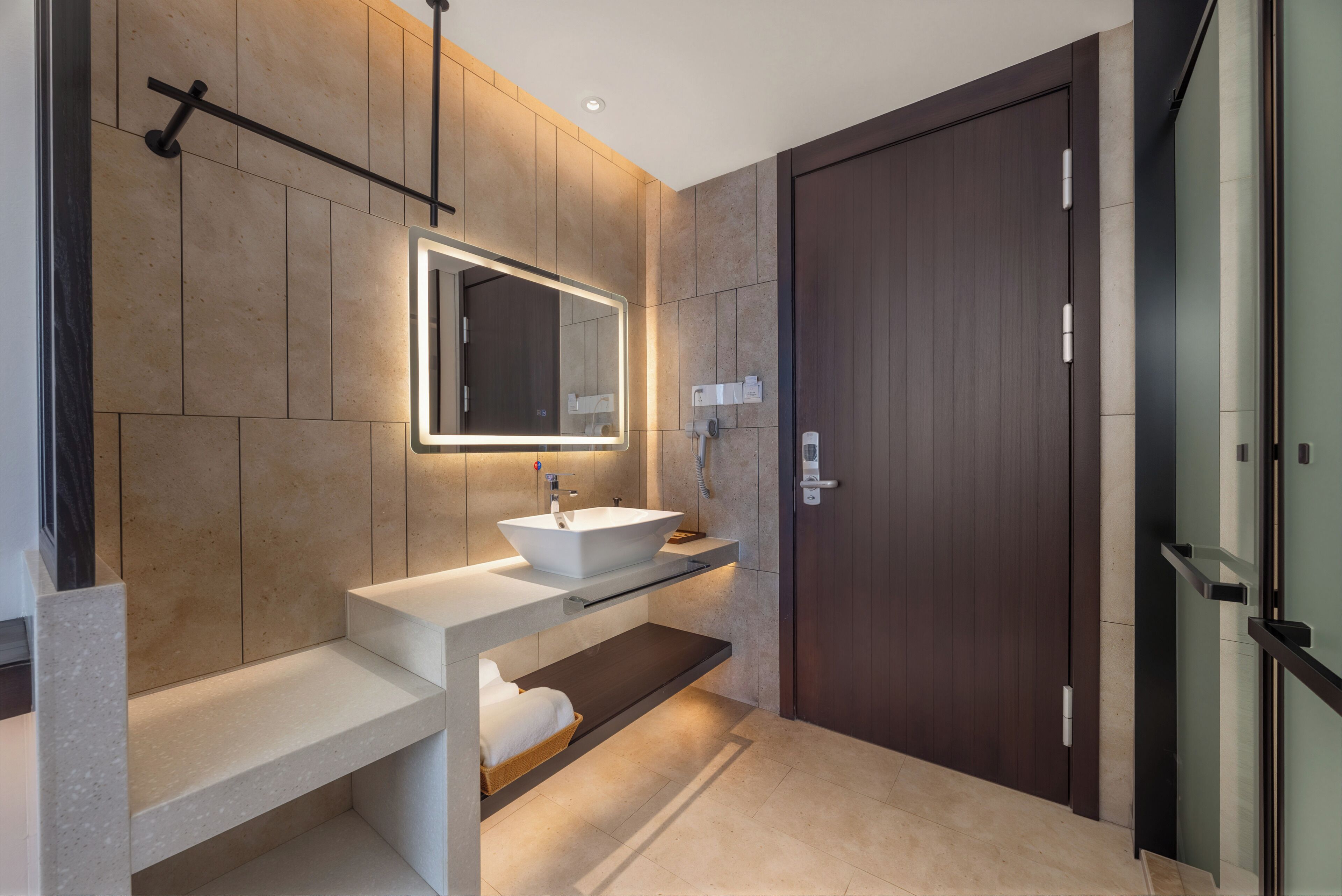 Une salle de bain moderne avec un grand miroir, un lavabo sur colonne et une porte en bois foncé.