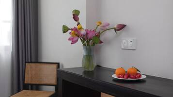 Una habitación con una mesa de madera oscura, un jarrón con flores, una silla y un plato con naranjas y cerezas.