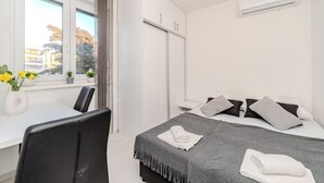 Habitació d'hotel amb llit, escriptori i cadira. Hi ha una finestra amb cortines i vista a edificis.