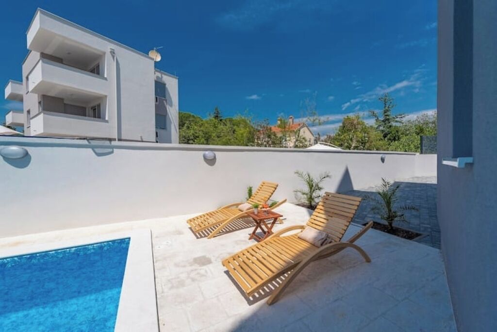 A modern building with a rooftop pool area featuring two wooden lounge chairs and a small table.