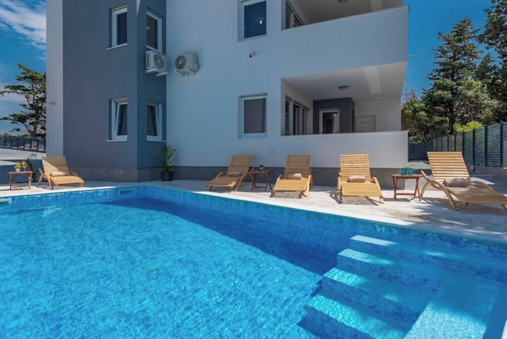 A modern building with a swimming pool and lounge chairs.