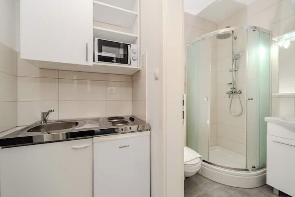 A modern bathroom with a glass-enclosed shower, a built-in microwave, and a sink with a stainless steel faucet.