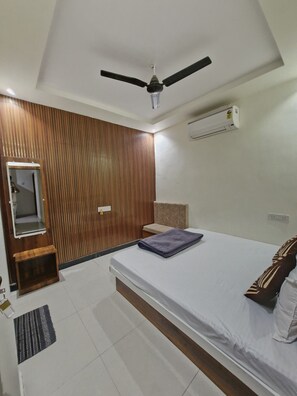 A bedroom with a bed, a ceiling fan, an air conditioning unit, a wooden panel wall, and a small wooden bench.