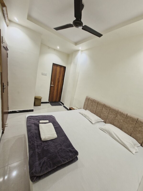 A hotel room with a bed, a ceiling fan, a wooden door, and a small stool.