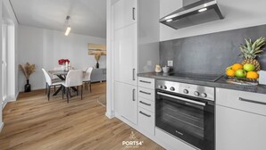 A modern kitchen with white cabinetry, a Bosch oven, and a dining area with a white table and chairs. - Ella - Terrace, 2 parking spaces, washing machine, fireplace, ground floor (Olpenitz)