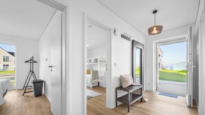 A modern, open-plan living space with a wooden floor, a bench, a hanging light fixture, and a view of the outdoors. - Ella - Terrace, 2 parking spaces, washing machine, fireplace, ground floor (Olpenitz)